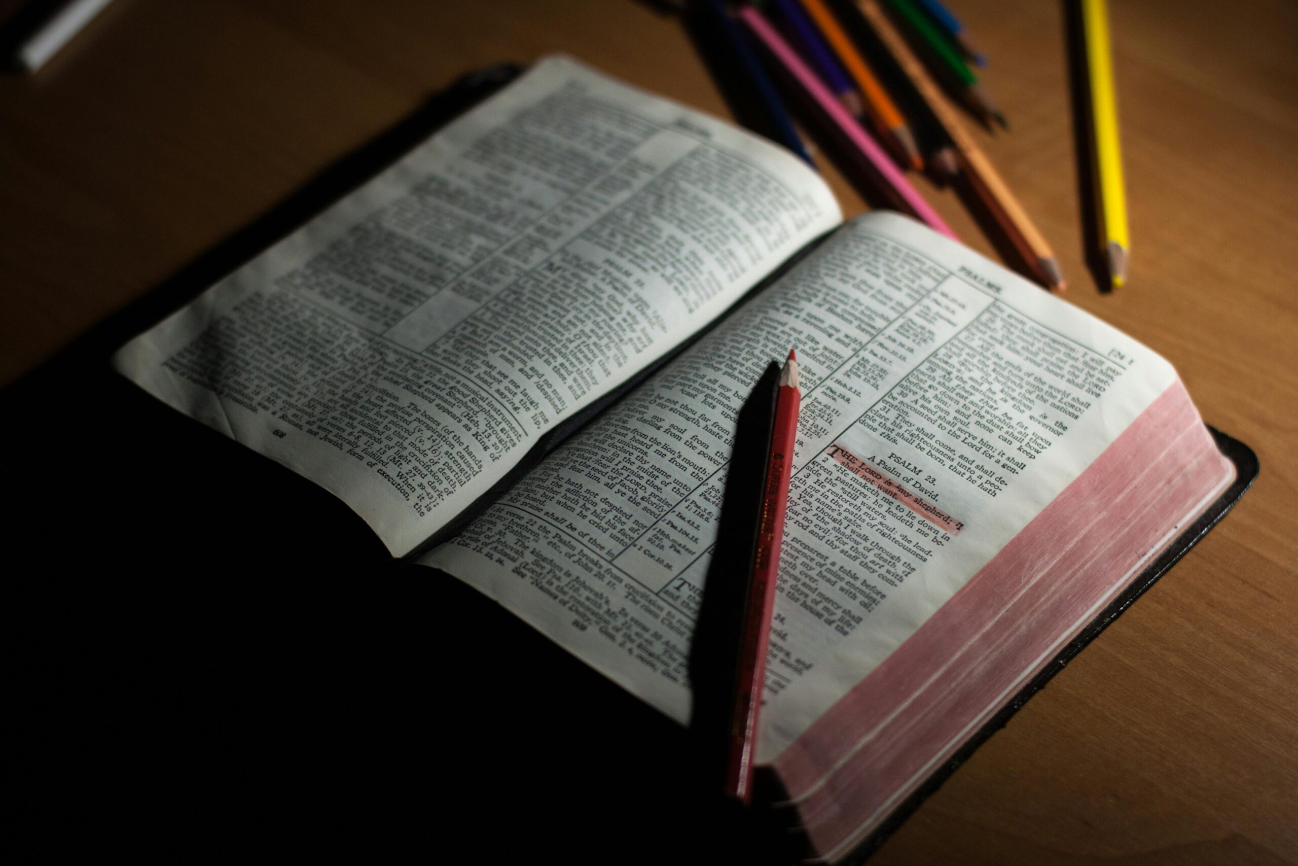 A bible sitting open at Psalm 23, with the first verse highlighted. A pencil is lying across the Bible, and there are more coloured pencils above it.