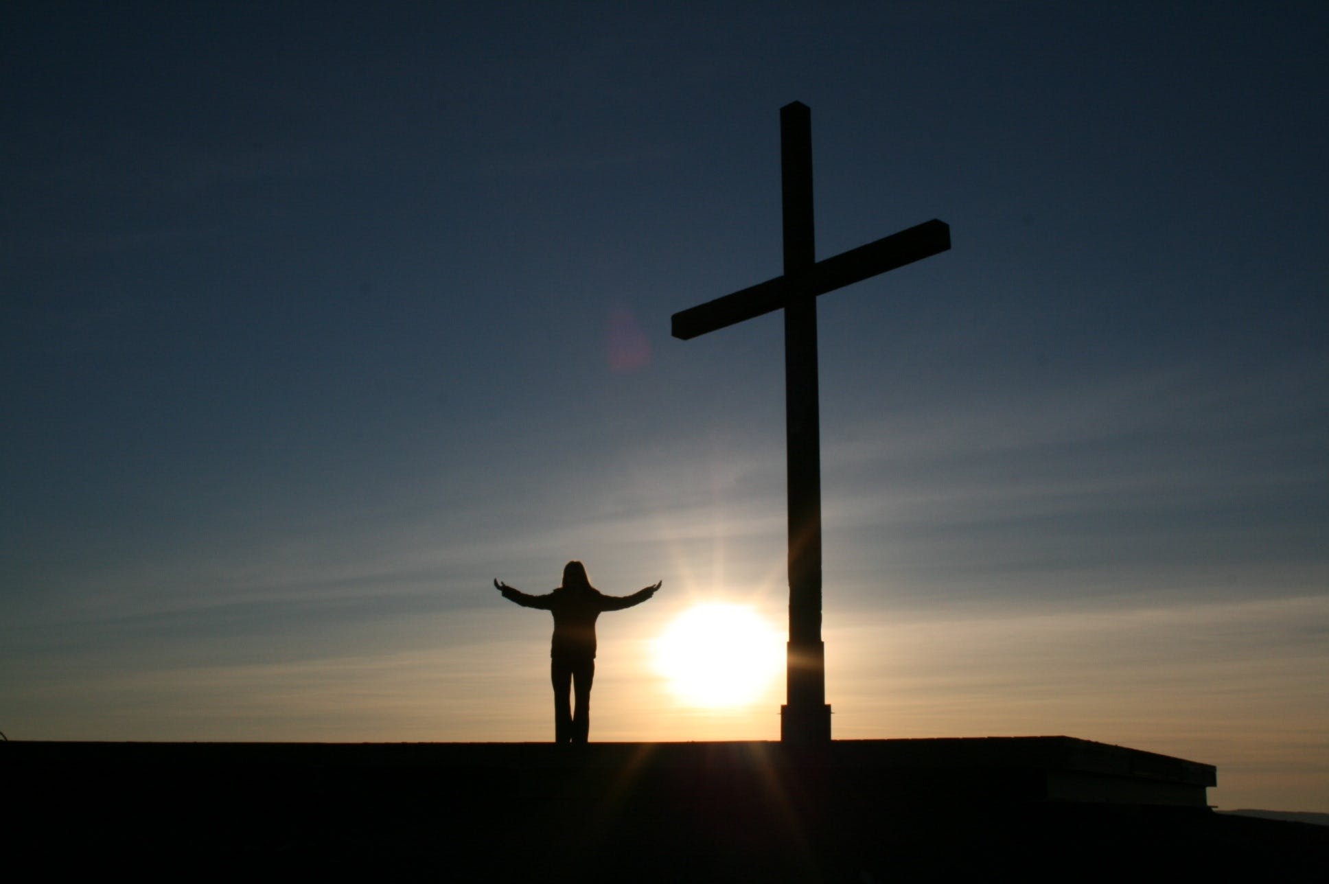 A person standing with their arms spread open beside a cross, representing them accepting Jesus as their Savior and getting to heaven.