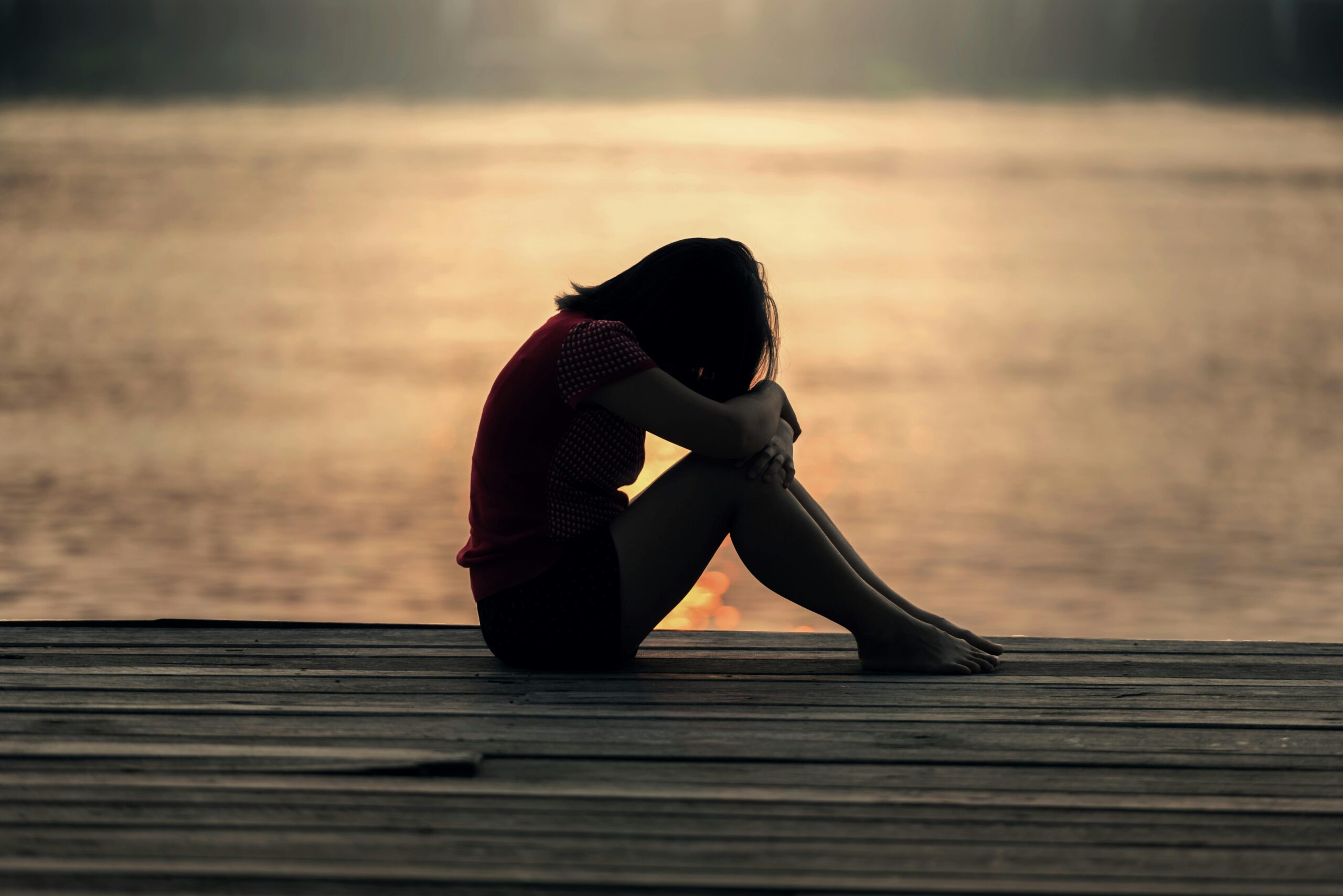 A woman sitting on a dock with her head in her hands, looking troubled.