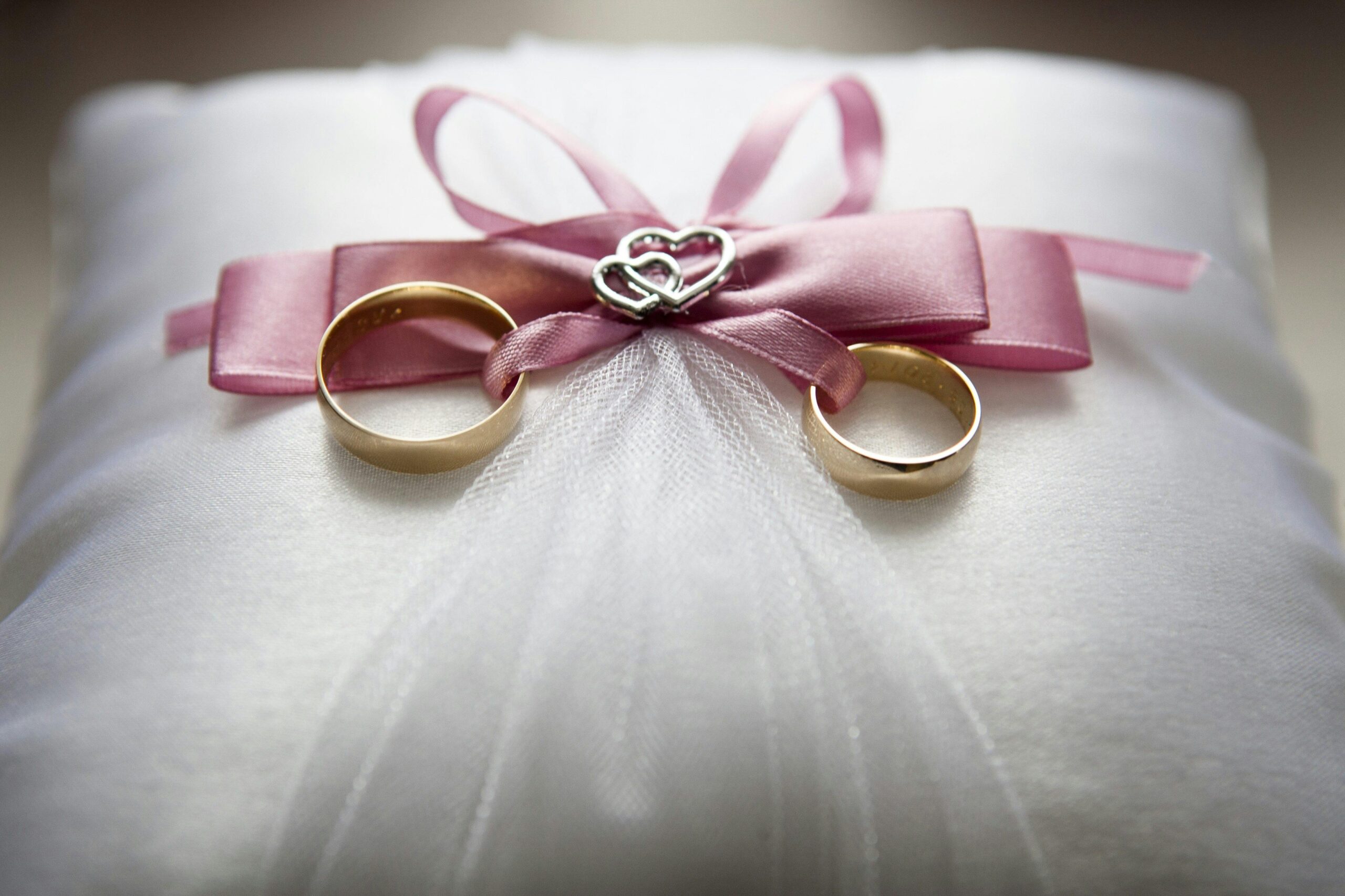Two marriage rings sitting on a cushion with a decorative bow, ready to be presented to the bride and groom.