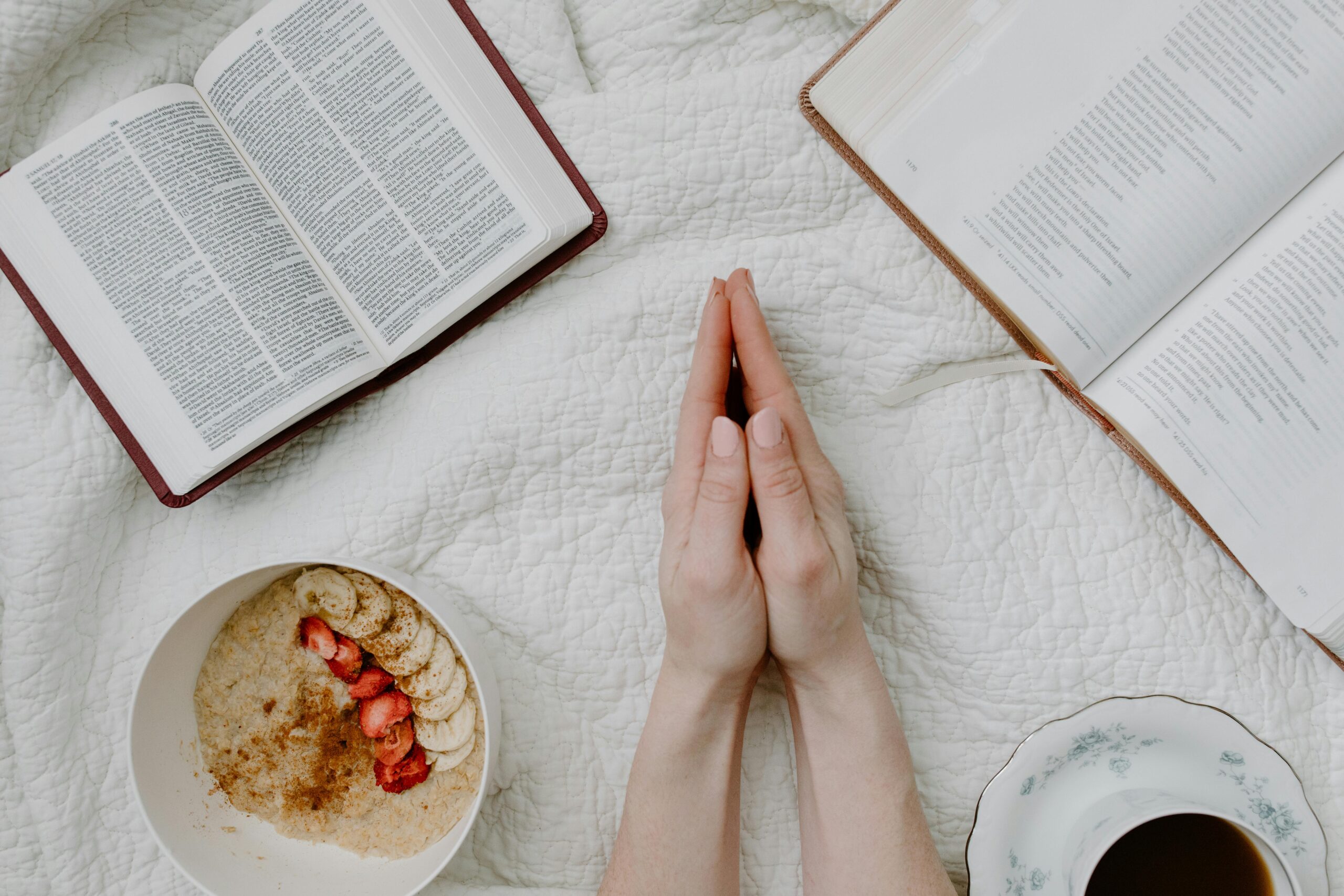 Hands folded in prayer with a Bible and a snack bowl on a table.